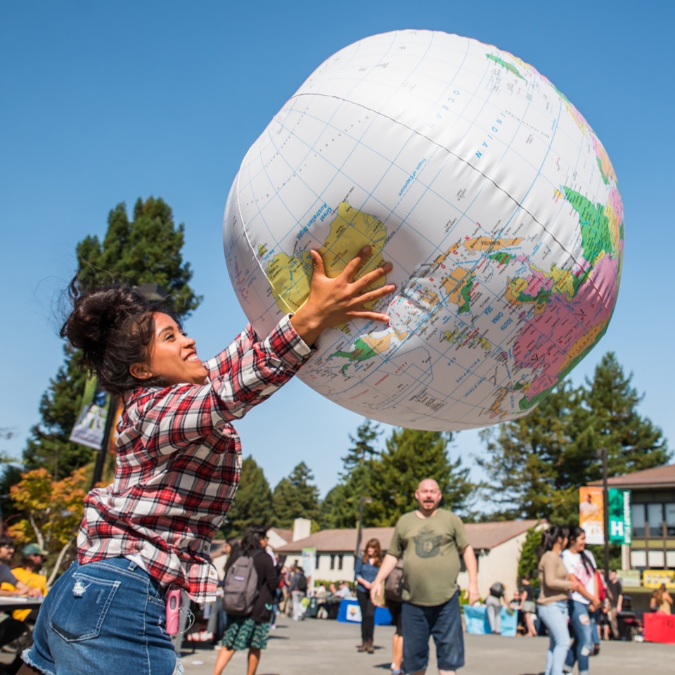 Student wearing a flannel shirt throwing a globe beach ball in the quad