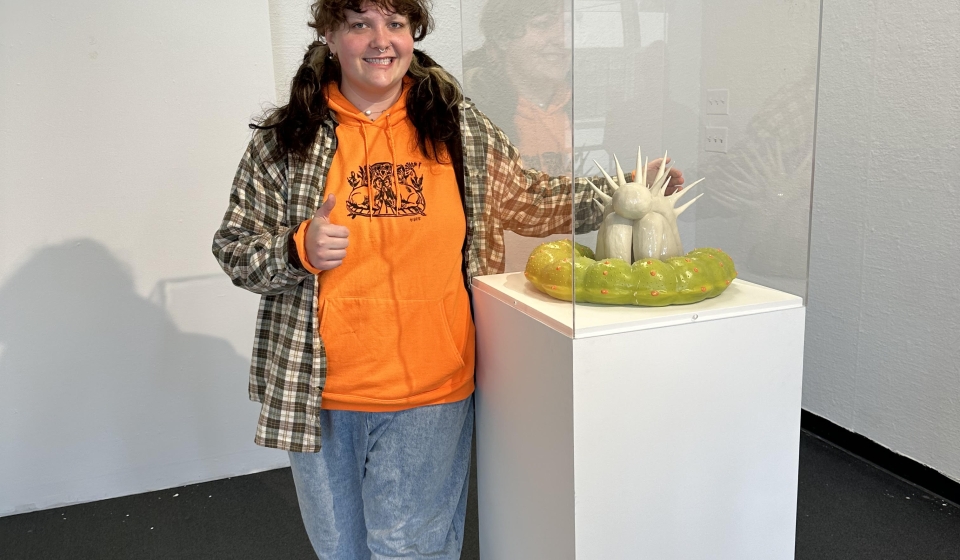 Art Student Li Jacobson standing with ceramic piece in display case.  Art piece accepted into CCACA 2023